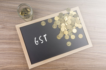 Coins in glass jar with GST word on chalkboard. Financial concept