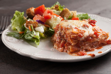 Homemade Italian four cheese lasagna with a side salad on a dark wooden background