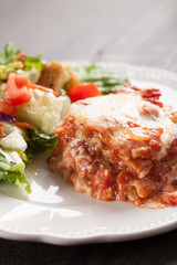 Homemade Italian four cheese lasagna with a side salad vertical shot