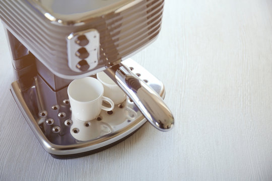 Modern coffee machine with cups on kitchen table, closeup