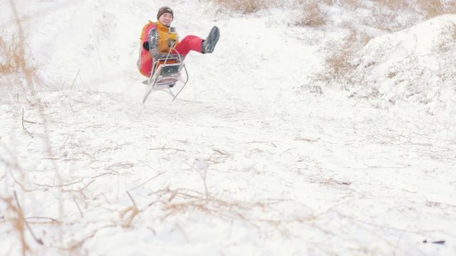 Guy riding sleigh down the hill at winter time and having fun, slow motion