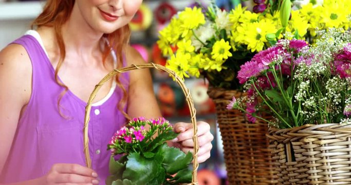 Beautiful female florist arraigning flower in wicker basket at flower shop