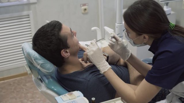 Young female dentist doctor making procedures with male patient, putting on protective gloves. Concept of healthy life