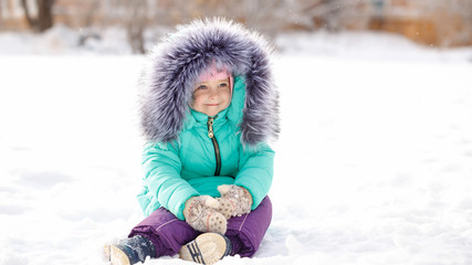 Pretty little girl in winter park. She is sitting in snow. Outdoor Activities. Close-up portrait