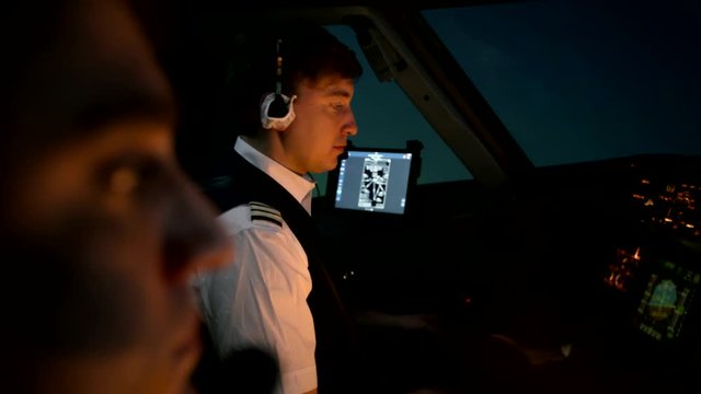 Close shot of professional pilots at the cabin of modern airliner. Aircraft begins to descent. Side view at the night time or early morning