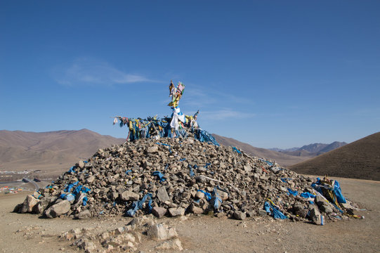 Ovoo made from stones worshipers have placed while praying. It is topped with a branch and many blue scarves and offerings. 
