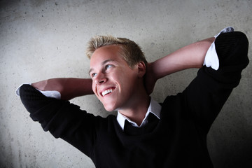 Teenage boy resting his head behind  his hands and smiling.