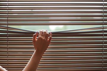 It's a sunny day outside. Woman's hand taking a peak through the window blinds.