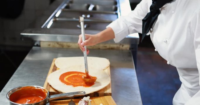 Chef applying sauce on flat bread while preparing pizza 4K