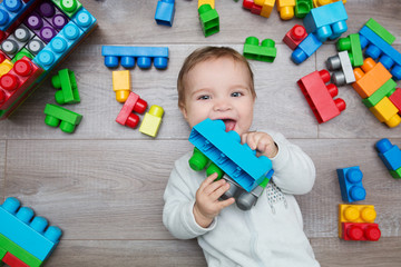 Little baby playing with lots of colorful plastic blocks constructor on floor in the room.