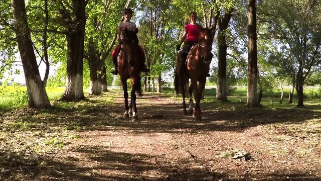 Two young girls riding horses in sunny spring day.