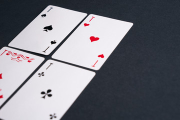 High Angle View of Four Playing Cards Spread Out on Dark Background Showing Aces from Each Suit - Hearts, Clubs, Spades and Diamonds