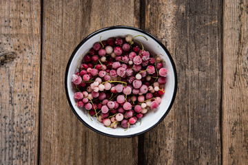 frozen berries, white currant and  red currant in enamel bowl  on wooden table in rustic style,  top view.