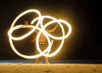 Long exposure shot of spinning burning torches in night fire show with vague silhouette of fakir...