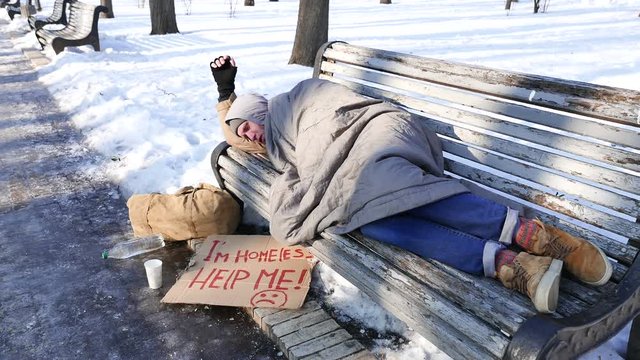 
4K. Homeless man sleeping on  bench in winter park. Slider shot
