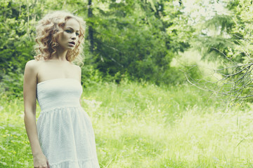 Beautiful young woman wearing elegant white dress standing in forest