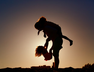 silhouette of father with two kids play at sunset sky