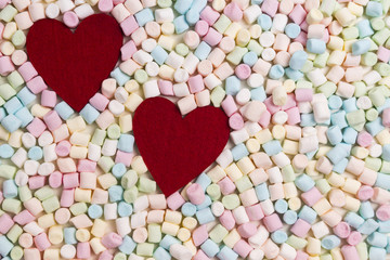 Two red hearts on colorful mini marshmallows background
