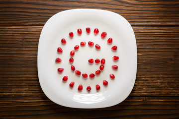 Pomegranate seeds in form of letter G on white plate on rustic w