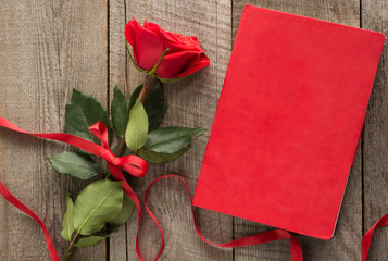 Valentine's card. Red rose and red notebook on wooden board. Top view.