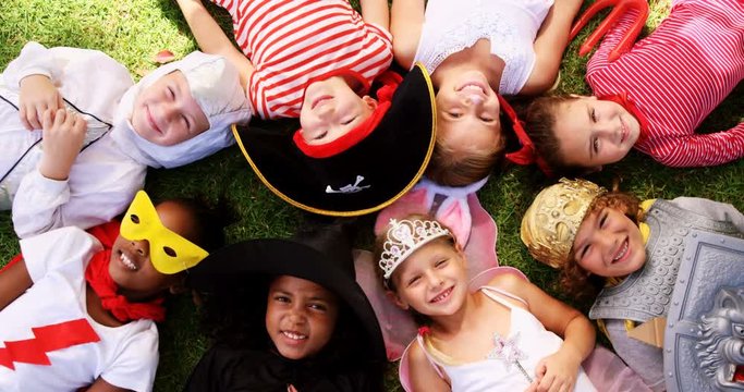 Portrait of group of kids in various costumes lying on grass in the park 4k