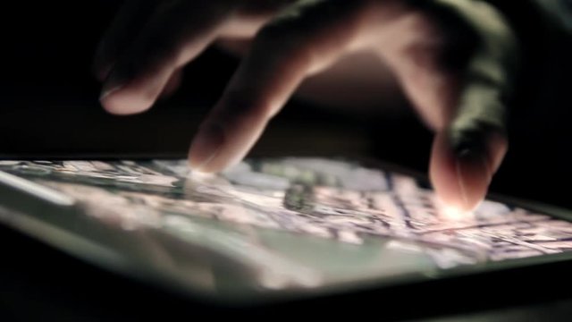 Browsing city map on tablet PC in the dark. Man's hand and screen close-up.