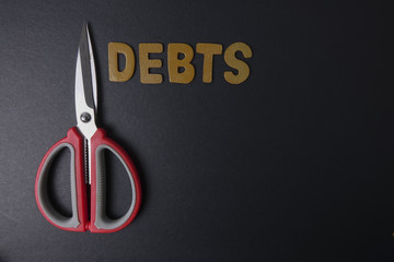 Scissors and word of DEBTS on black background. Business concept