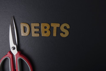 Scissors and word of DEBTS on black background. Business concept