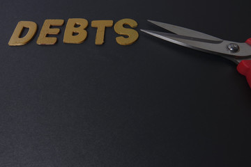 Scissors and word of DEBTS on black background. Business concept