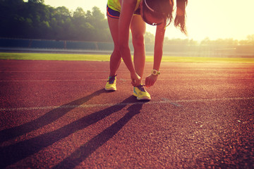 young fitness woman runner tying shoelace on stadium track