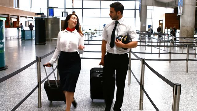 Pilot and female flight attendant walking with luggage at airport