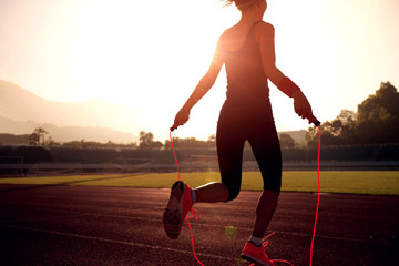 Young woman skipping rope during sunny morning on stadium track - obrazy, fototapety, plakaty