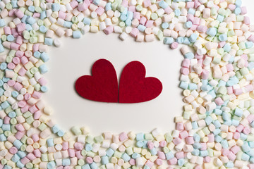 Obraz premium Two red hearts in the frame of colorful mini marshmallows as background