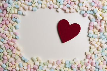Red heart in the frame of colorful mini marshmallows as background. Top view
