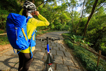 young woman cyclist adjust the helmet belt before riding mountain bike on forest trail - Powered by Adobe