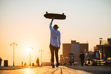 Young hipster man walking with longboard in hands on the boardwalk outside