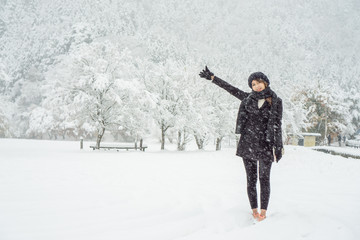 Young Asian girl standing in the heavy snow with white background of snow covered tree and mountain 