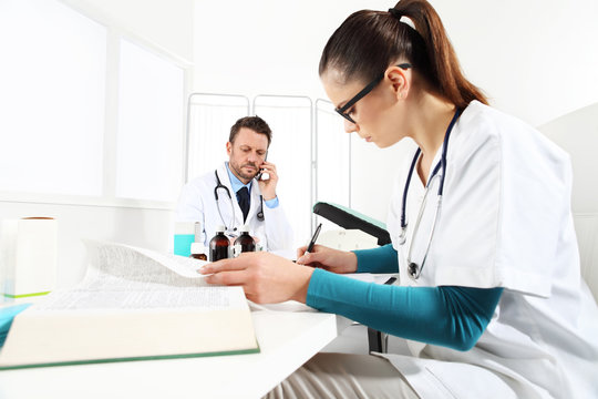 Doctor at mobile phone and nurse read medical book in office