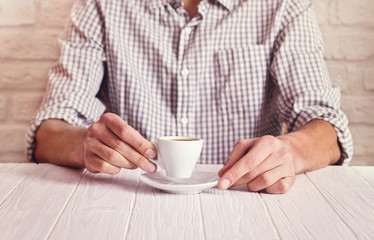Coffee break. Man sitting on the white table with cup of espresso in the checked shirt. White bricks wall background