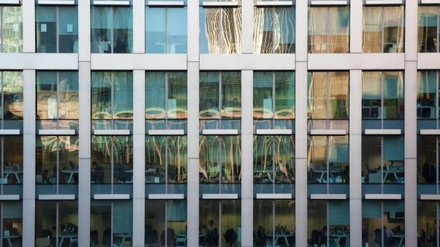 Time lapse of the exterior of a modern office block in the afternoon showing the daily activity of office workers themes of routines working late deadlines