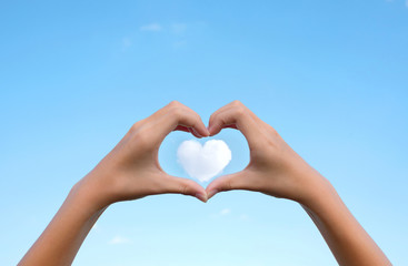 Fototapeta premium Asian young girl hands holding hands in heart shape framing on cloud heart shape with clear blue sky background for Happy valentines day or wedding concept and copy space.