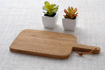 Empty wooden chopping board and small tree pots on sack tablecloth, food display montage background
