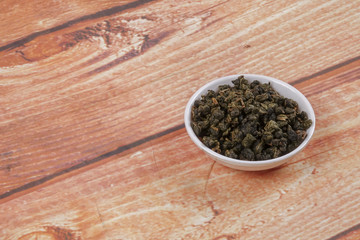 dried chinese tea leaves in a small bowl over wooden background