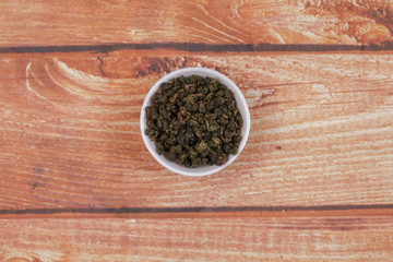 dried chinese tea leaves in a small bowl over wooden background