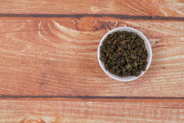 dried chinese tea leaves in a small bowl over wooden background
