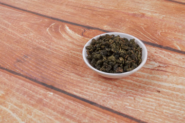 dried chinese tea leaves in a small bowl over wooden background