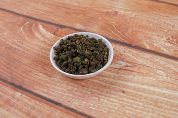 dried chinese tea leaves in a small bowl over wooden background
