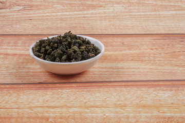 dried chinese tea leaves in a small bowl over wooden background