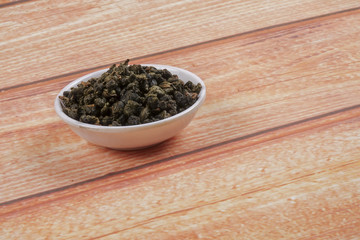 dried chinese tea leaves in a small bowl over wooden background