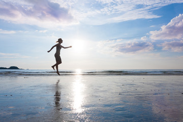 Woman is jumping to sky on beautiful sunset sea beach with wet sand. Free power mind or meditation and zen concept.